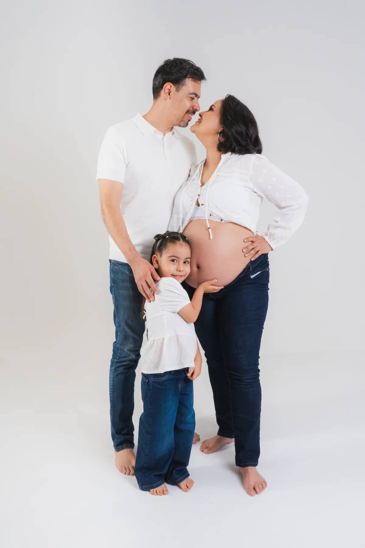 Pareja besándose con su hija abrazando la barriga