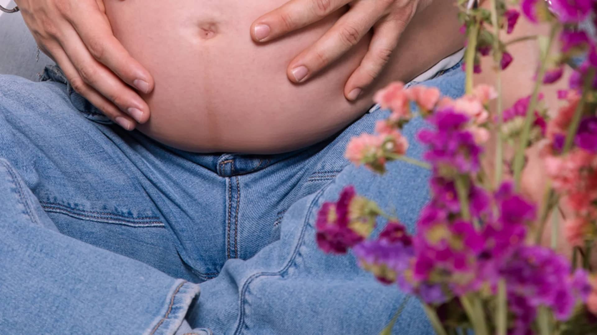 Barriga de embarazada con las manos de la pareja y flores